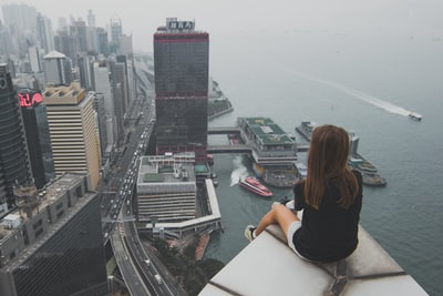 白天坐在楼顶上俯瞰海湾边城市的女人